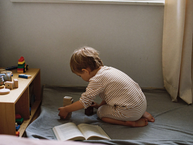 A child kneeling on the floor, stacking wooden blocks on their own